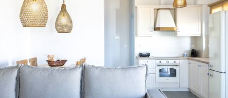 A modern kitchen with white cabinets, a built-in oven, and a refrigerator. There is a grey sofa with cushions in the foreground.