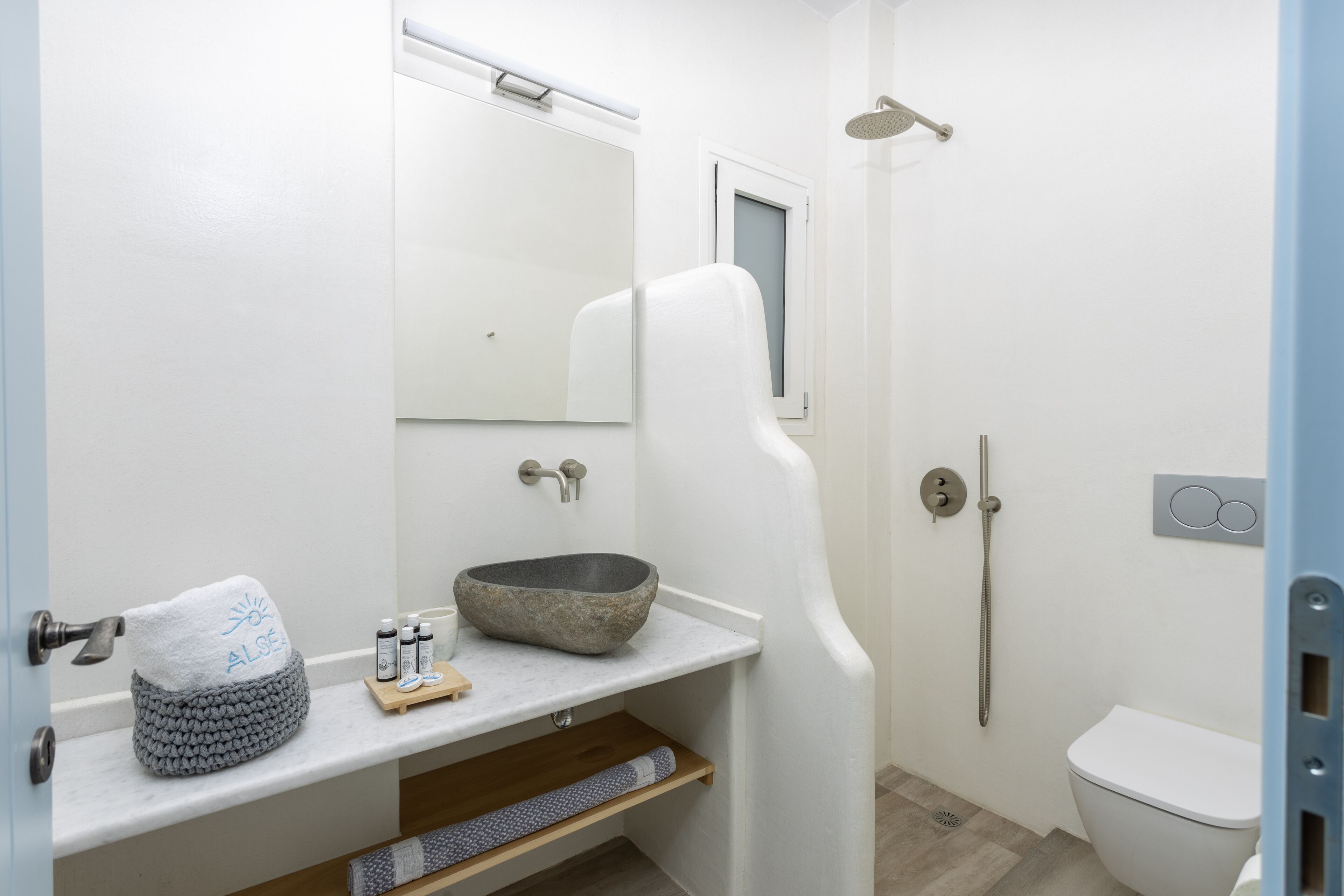 A modern bathroom with a white sink, a stone basin, a towel, and a shower.
