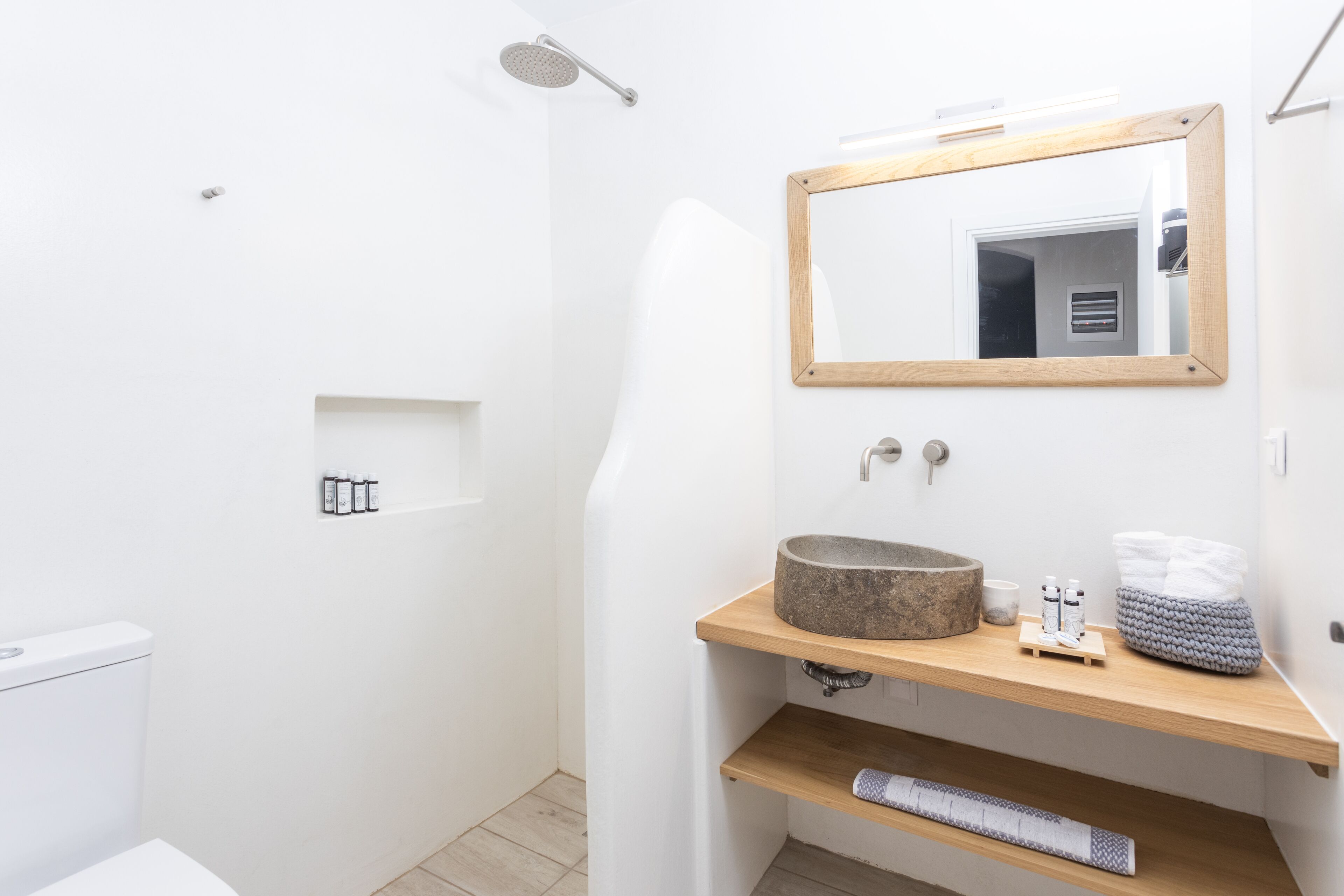 A modern bathroom with a white sink, a wooden vanity, a large mirror, and a shower area.