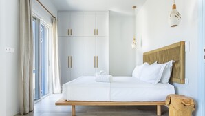 Une chambre moderne avec un grand lit, une tête de lit en bois et un petit tabouret en bois.
