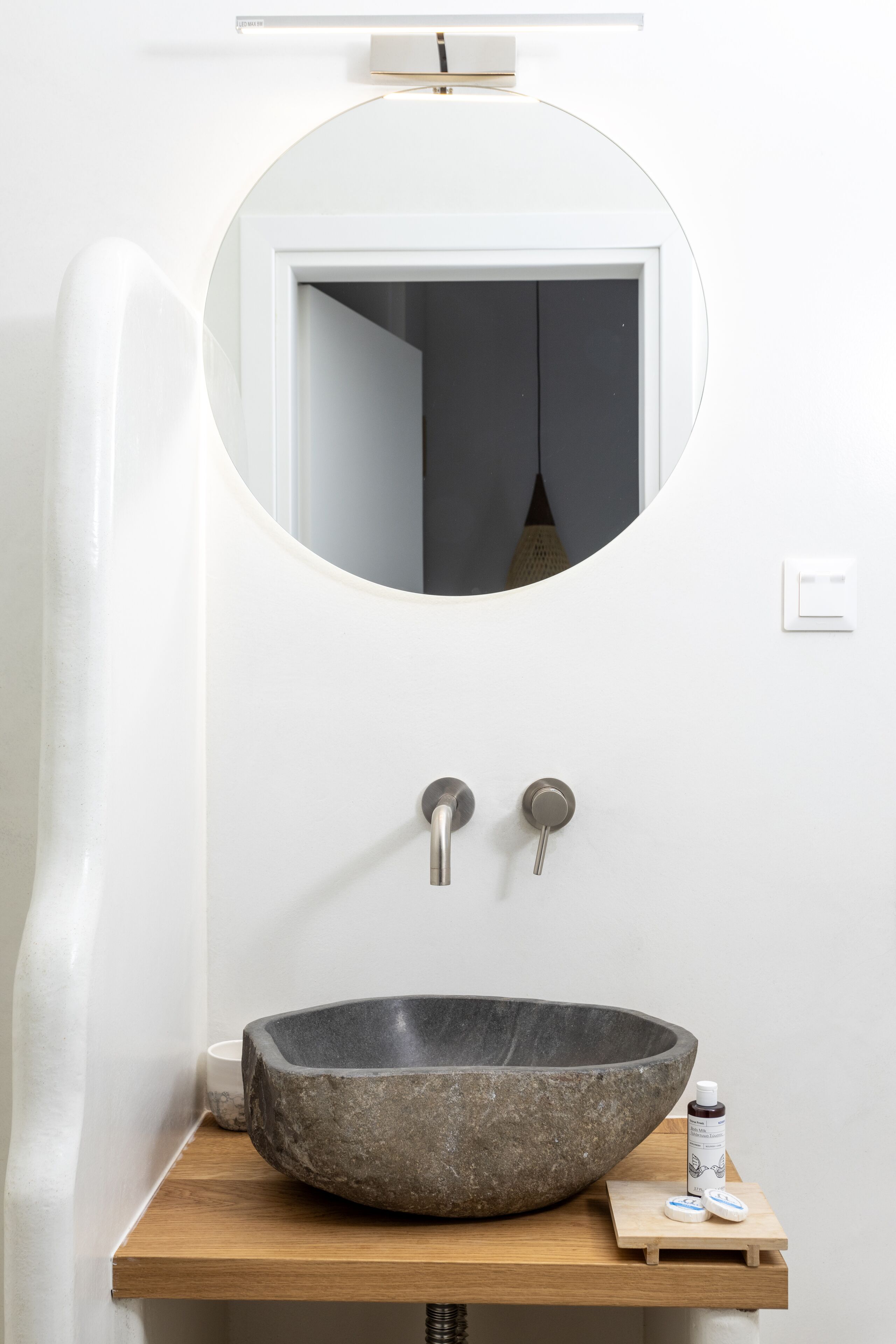 A bathroom with a round mirror, a stone sink, and a wooden shelf.