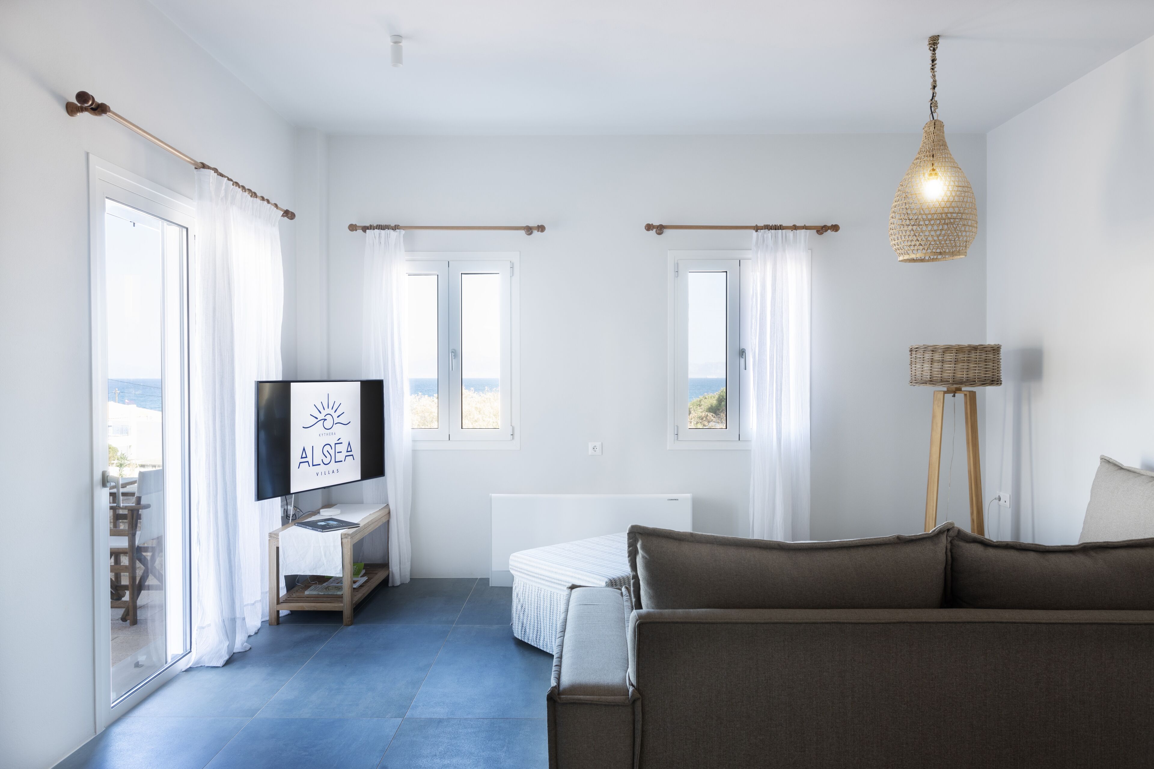 Un salon moderne avec un canapé, un téléviseur, une lampe sur pied et une vue sur la mer grâce à de grandes fenêtres.