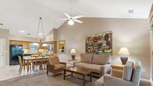 A living room with a sofa, chairs, a coffee table, a dining area with a table and chairs, a kitchen in the background, and a ceiling fan. - Golf Condo at StoneBridge only Minutes from Silver Dollar City (Reeds Spring)