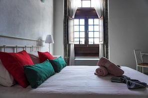 A bed with pillows, a rolled towel, and a pair of slippers.