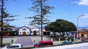 Une église dotée d’un clocher, d’une cour pavée et d’une rue bordée de voitures garées.