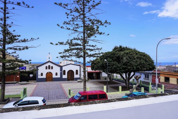 Una iglesia con un campanario, un patio empedrado y una calle con coches aparcados.
