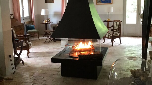 Una sala de estar con chimenea, una mesa de vidrio con un objeto decorativo y un sillón.