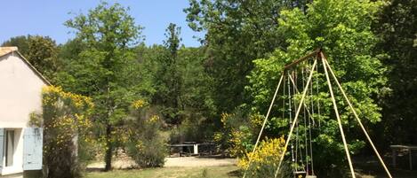 A backyard with a swing set, a small shed, and a house with a white exterior.