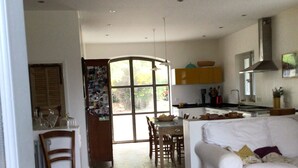 Un amplio salón con un sofá blanco, una mesa de comedor con sillas y una zona de cocina con estufa y armarios.