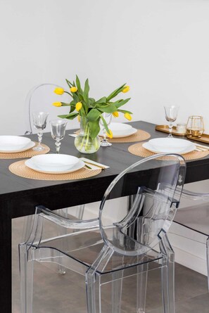 A dining table set with white plates, clear glassware, and a vase with yellow flowers.
