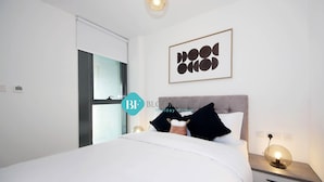 A modern bedroom with a large bed, a nightstand with a lamp, and a framed artwork on the wall. - Luxury duplex in Raha lofts (Abu Dhabi)