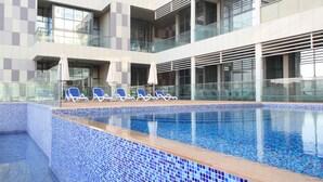 A modern indoor pool with blue mosaic tiles, lounge chairs, and glass railings. - Luxury duplex in Raha lofts (Abu Dhabi)