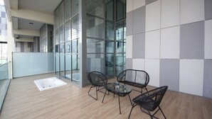 A balcony with a wooden floor, glass walls, and a seating area with chairs and a table. - Luxury duplex in Raha lofts (Abu Dhabi)