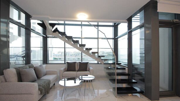 A modern living room with a sofa, coffee table, and a staircase leading to an upper floor. - Luxury duplex in Raha lofts (Abu Dhabi)