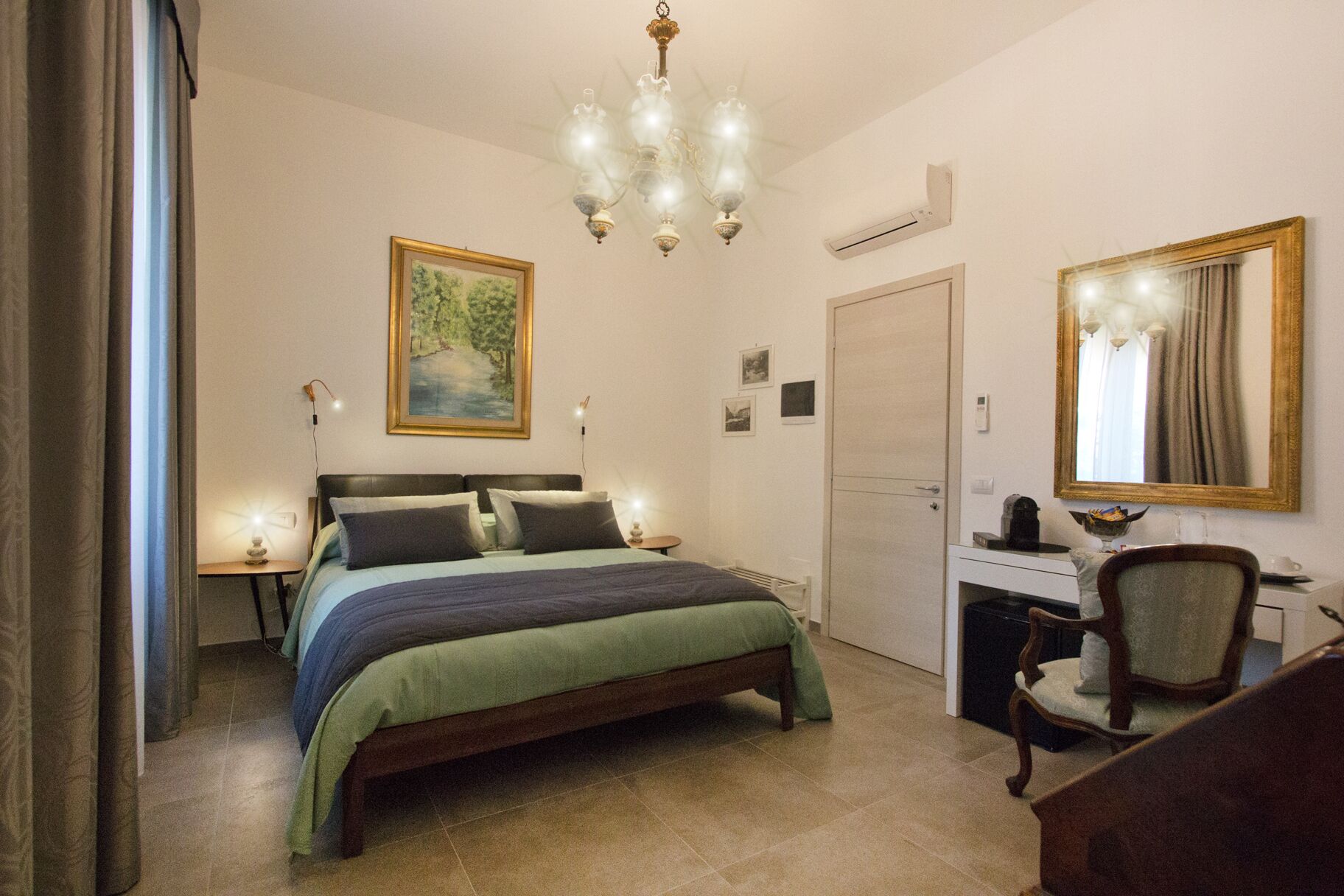 A bedroom with a bed, a desk, a chair, a mirror, a chandelier, and a painting on the wall.