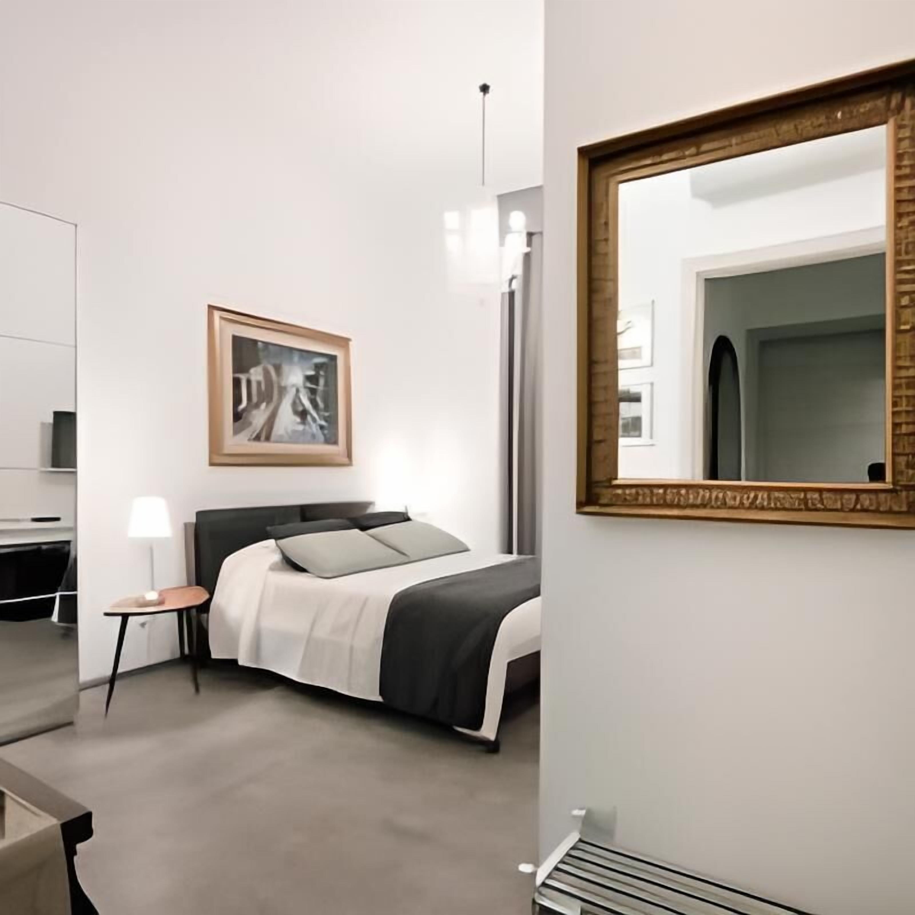 A modern hotel room with a bed, bedside table, lamp, and a framed abstract painting on the wall.