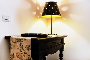 A lamp on a table with a floral tablecloth, a small drawer, and a wall socket. - IMHOME - Porta Romana (Milan)