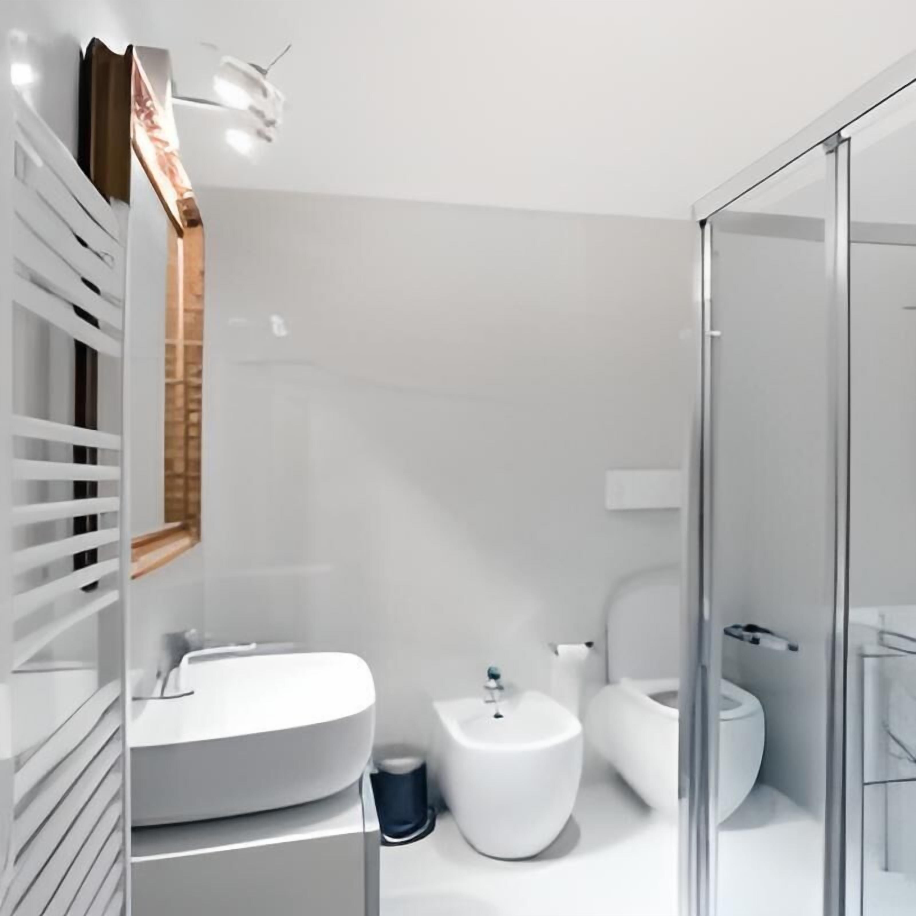Une salle de bain moderne avec un lavabo, des toilettes et un bidet, tous de couleur blanche. On y trouve une douche en verre et un miroir avec un cadre en bois.