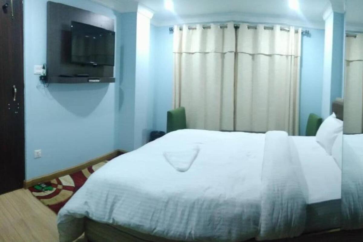A hotel room with a bed, a television mounted on the wall, and curtains on the windows.
