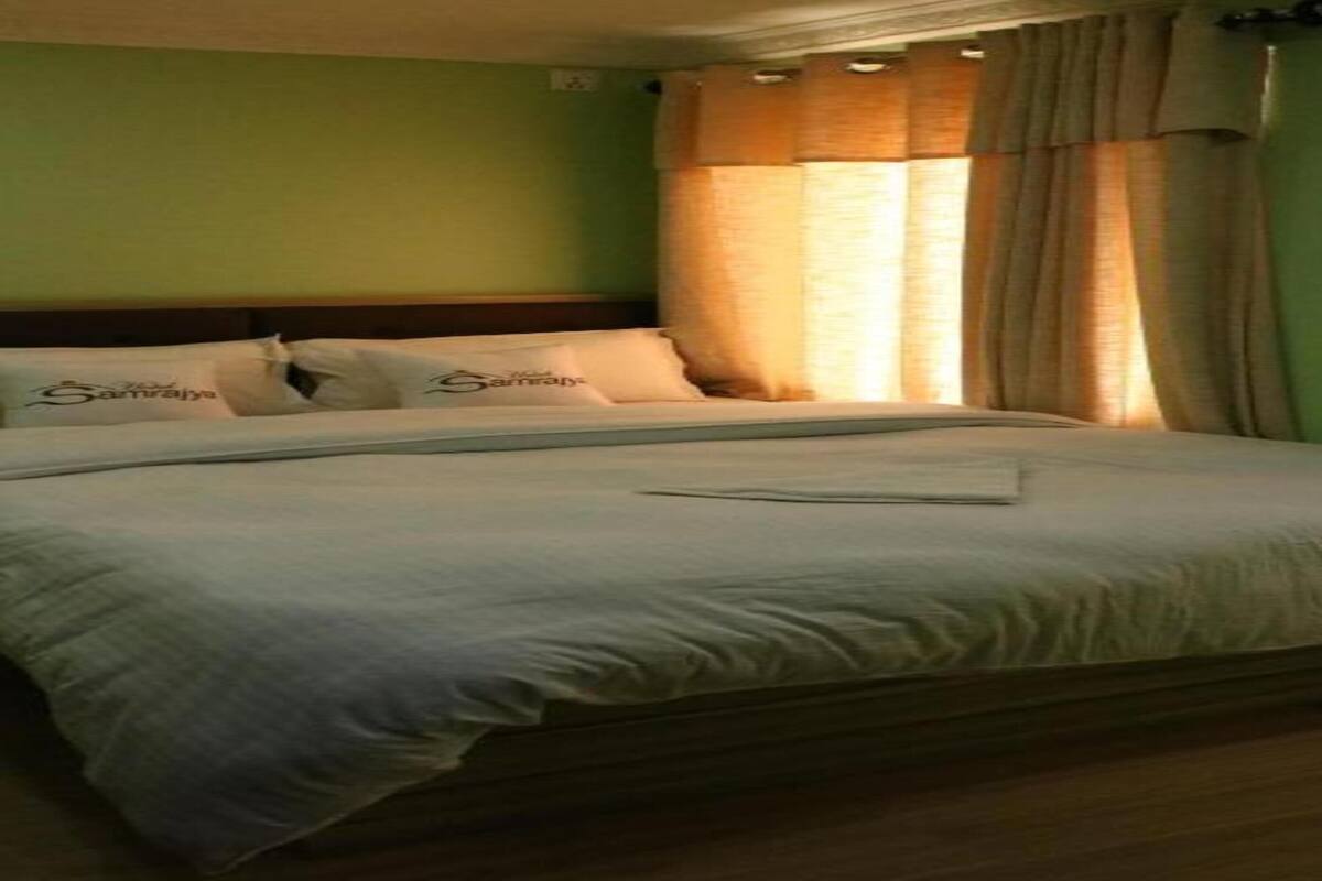 A neatly made bed with white bedding and pillows, a wooden headboard, and a window with curtains.