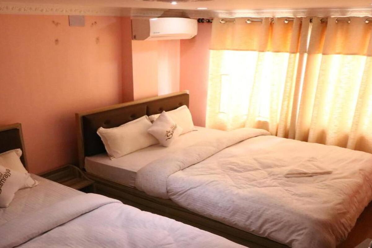 A hotel room with two beds, a window with curtains, and an air conditioning unit on the wall.
