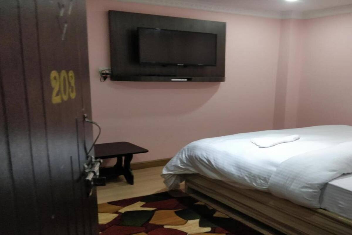 A bedroom with a bed, a television mounted on the wall, and a door with a number.