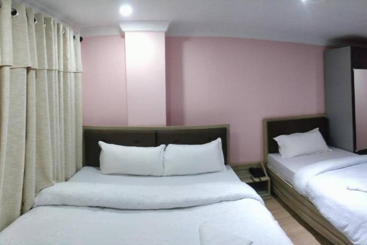 A room with two beds, a wooden headboard, a light switch, and a door.