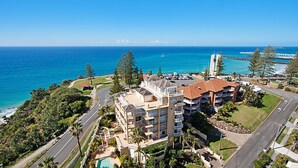 A coastal hotel with multiple balconies, a swimming pool, and a view of the ocean and bridge.
