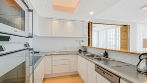 A modern kitchen with white cabinetry, a built-in oven, a microwave, a sink, and a large mirror.