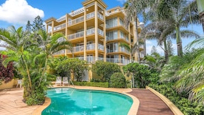 A multi-story hotel with a swimming pool surrounded by lush greenery and palm trees.