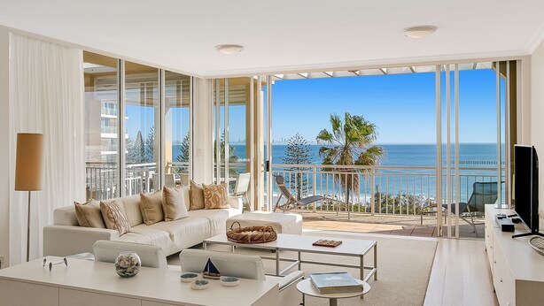 A modern living room with a large window overlooking a beach and cityscape.