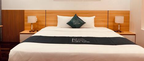A hotel room with a wooden headboard, a bed with white bedding, two bedside lamps, and three wall-mounted floral paintings.