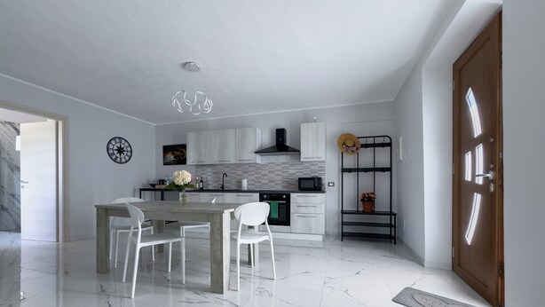 A modern kitchen with white cabinets, a marble floor, and a dining area with white chairs. - TRAMONTO, Roero Sunset (Govone)