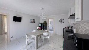 A modern kitchen with a dining area, white marble flooring, a flat-screen TV, and a clock on the wall. - TRAMONTO, Roero Sunset (Govone)