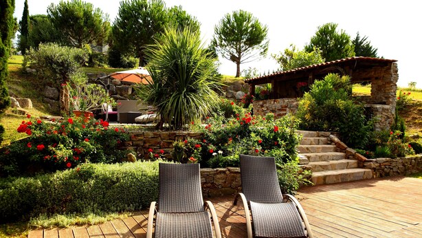 Une terrasse avec deux fauteuils en osier, un escalier en pierre et un jardin agrémenté de diverses plantes et fleurs.