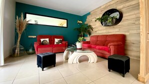 Un salon aux murs de couleur turquoise, avec un canapé rouge, une table basse en verre et un mur décoratif en bois.