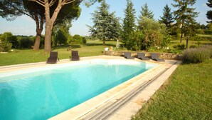 Une piscine rectangulaire bordée de pierres, entourée d’une pelouse et d’arbres.