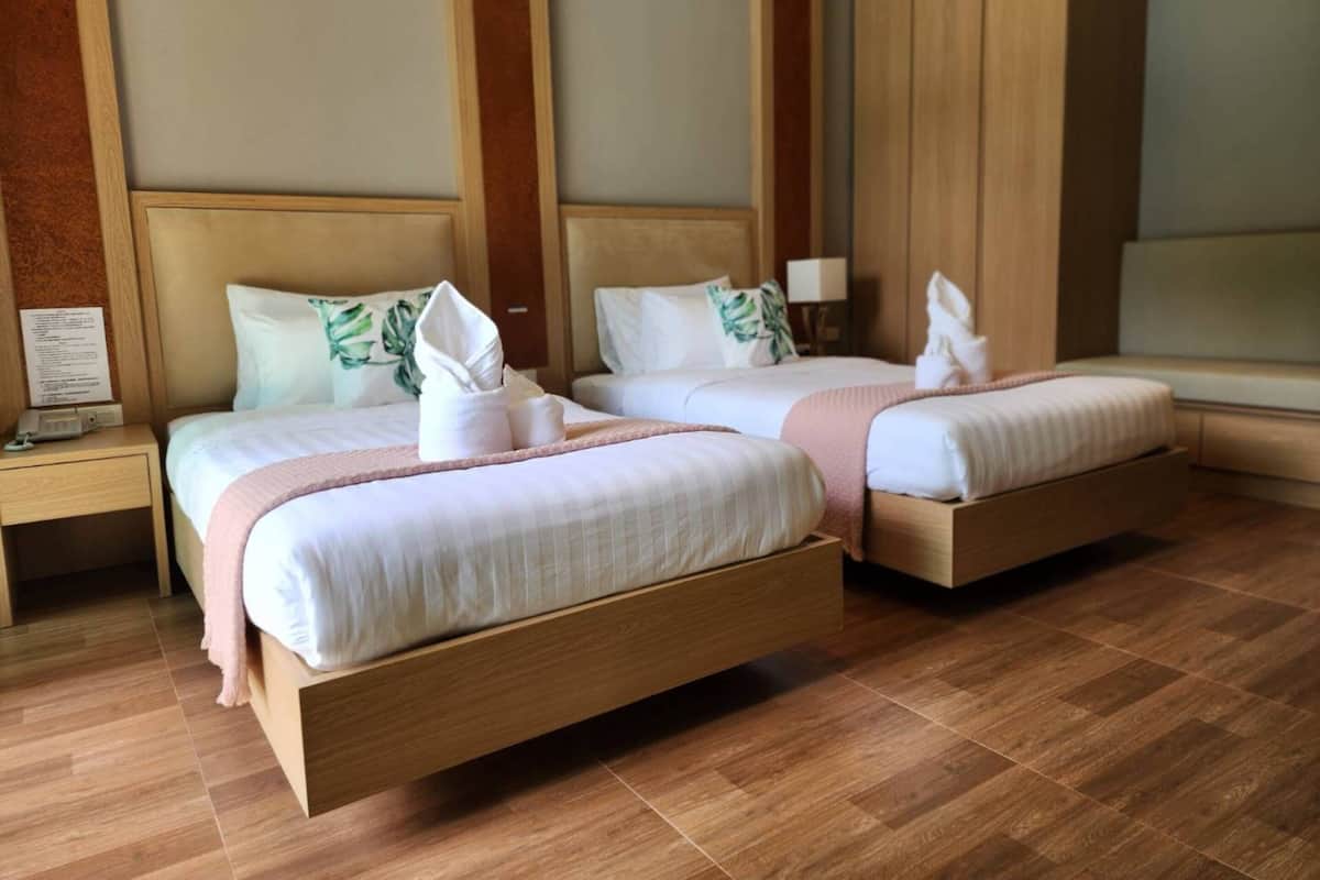 A hotel room with two beds, wooden headboards, a nightstand with a lamp, and a large window.