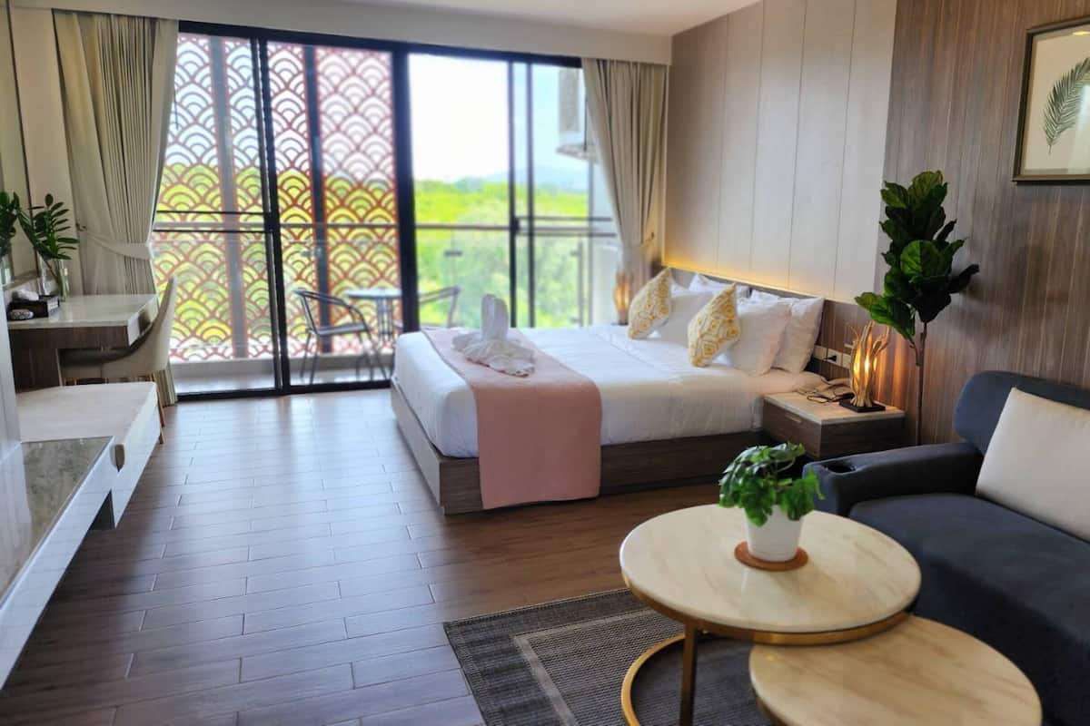 A modern hotel room with a bed, a sofa, a small table, and a balcony with a view.