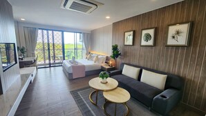 Una habitación de hotel moderna con cama, sofá, dos mesas redondas, un balcón con vistas y obras de arte enmarcadas en la pared.