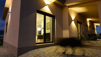 A modern building with a glass door entrance, outdoor seating area, and a stone-paved patio.