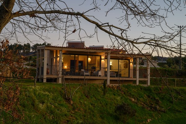 Ein modernes Haus mit überdachter Veranda und zahlreichen Fenstern, umgeben von viel Grün.