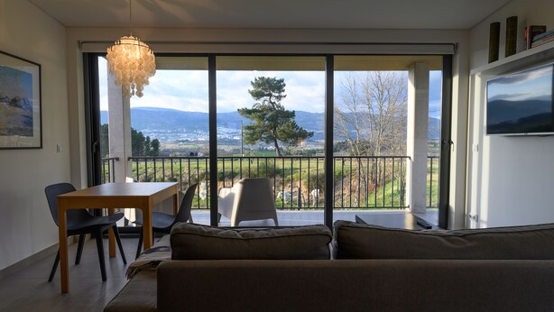 A modern living room with a large window, a dining area with a table and chairs, and a sofa. - Laje da Bica Agroturismo (Covilha)