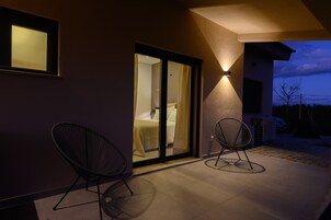A modern exterior with a glass door leading to a bedroom, two chairs, and a wall-mounted light fixture.
