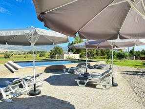 Ein Poolbereich mit Liegestühlen und Sonnenschirmen, ein Schwimmbecken und Blick auf die Landschaft.