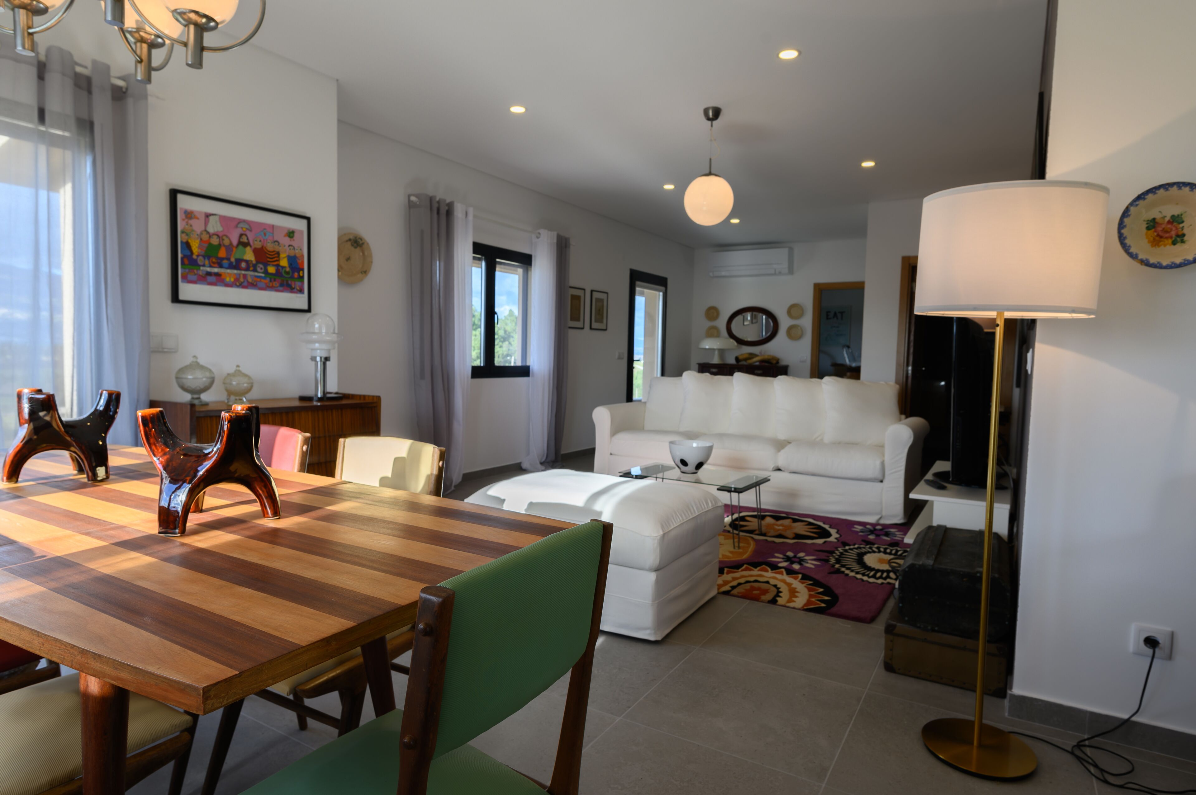 Un salon moderne avec une table à manger en bois, un canapé blanc et un tapis coloré.