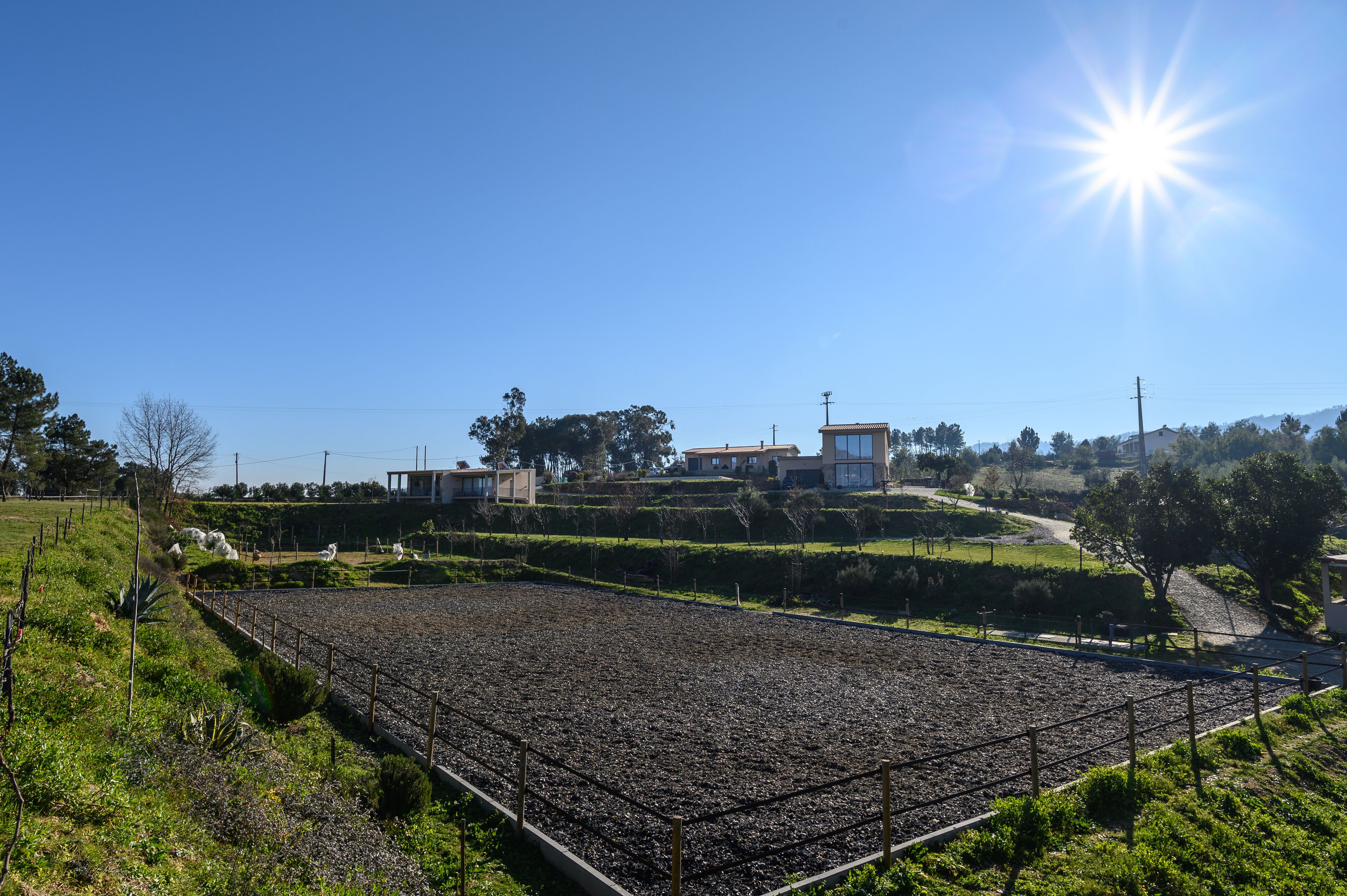A rural landscape with a large open field, a few buildings, and a clear sky.