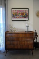Un mueble de madera con cristalería y un cuadro enmarcado encima.