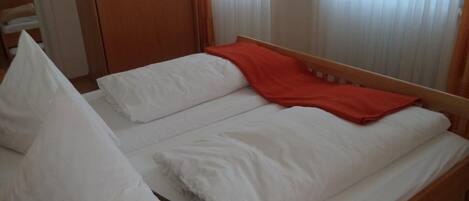 A single bed with white bedding and a red blanket, a wooden headboard, and a wooden wardrobe in the background.