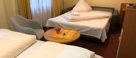A hotel room with two beds, a desk, a chair, and a small table with a cup and saucer.